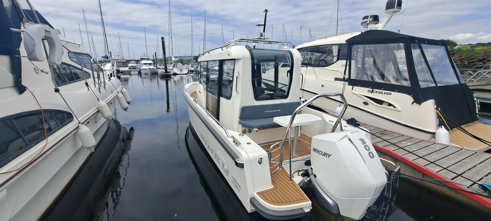 A Nimbus boat docked at a marina, with a Mercury 300 engine, surrounded by other moored yachts under a cloudy sky.